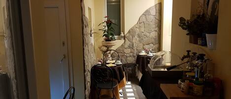 A narrow hallway with a stone wall, a door, a small table with a chair, a potted plant, and a sink with a faucet.