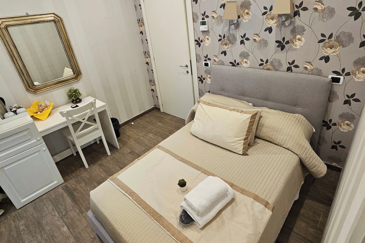A bedroom with a bed, bedside table, and a mirror.