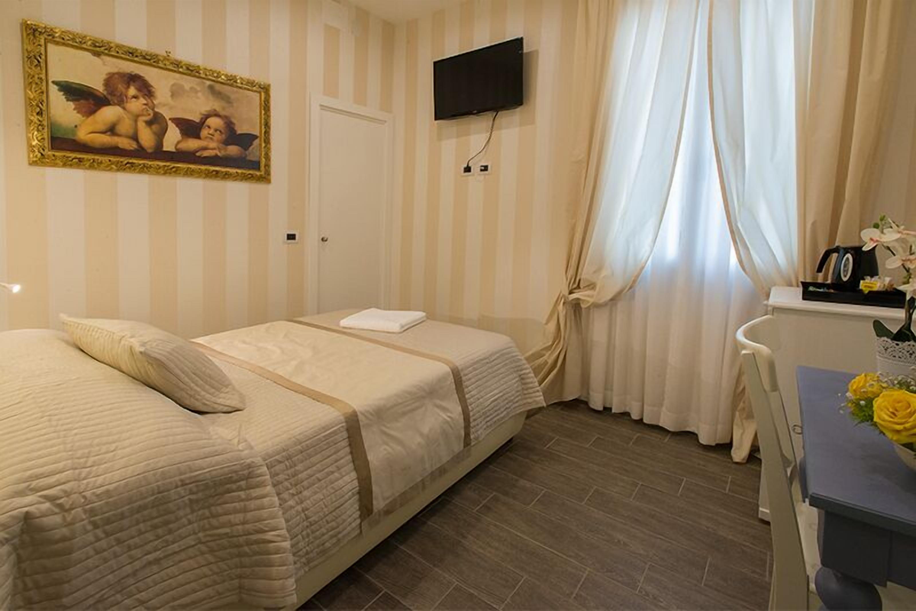 A hotel room with two beds, a TV mounted on the wall, a desk with a chair, and a window with curtains.