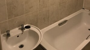 A bathroom with beige tiles, a sink, and a bathtub. - Rooms at 5 Hammersmith Road - Hostel (London)