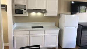 A compact kitchen with white cabinetry, a microwave, a built-in oven, and a refrigerator. - Luxury Inn & Suites (Houston)