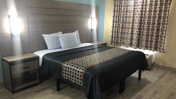 A hotel room with a bed, bedside tables, a desk, and a patterned curtain. - Luxury Inn & Suites (Houston)