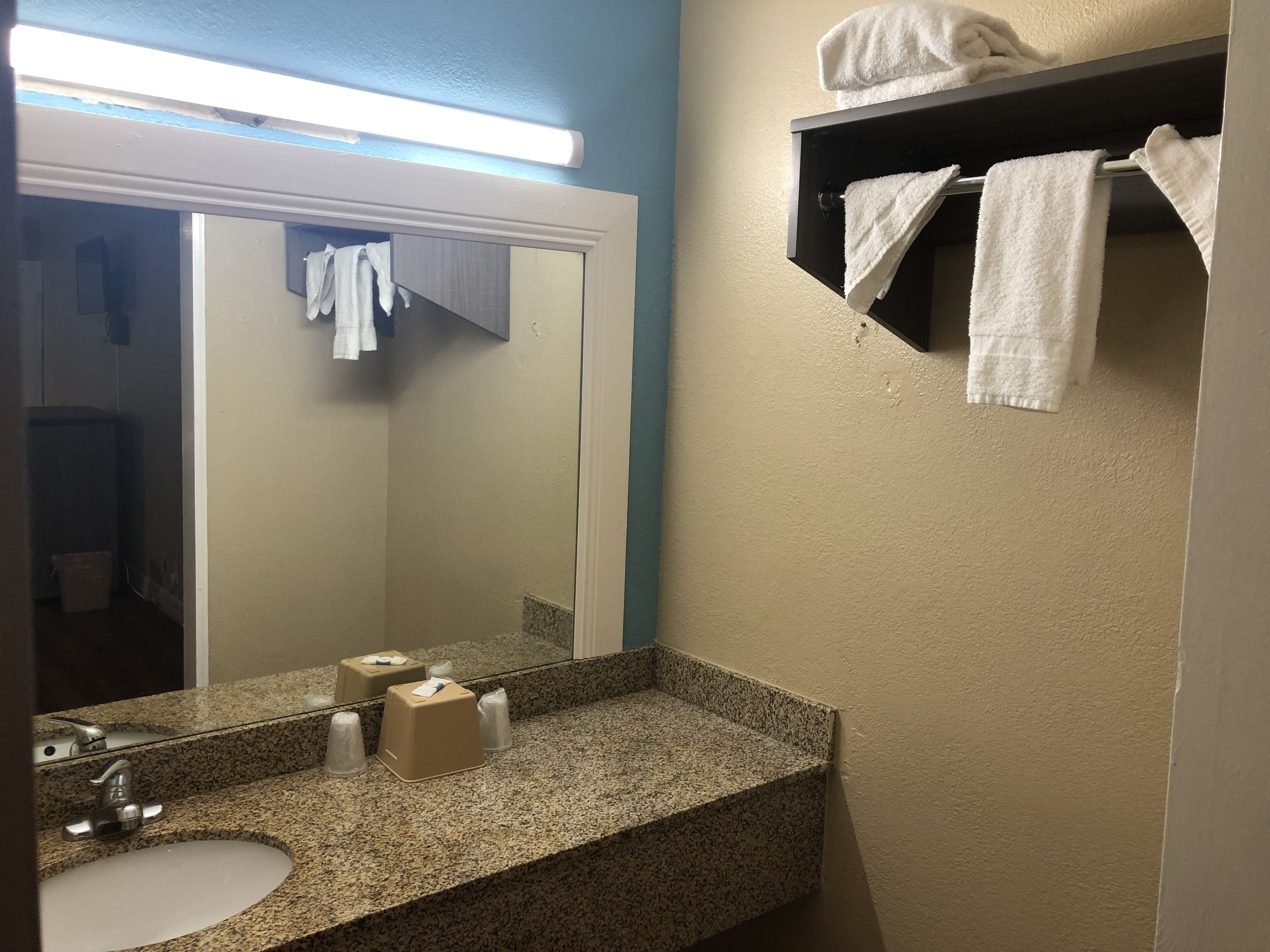 Un baño con encimera de granito, un lavabo, un espejo y un perchero con toallas.