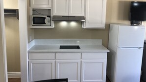 A compact kitchen with white cabinets, a microwave, a stove, and a refrigerator. - Luxury Inn & Suites (Houston)