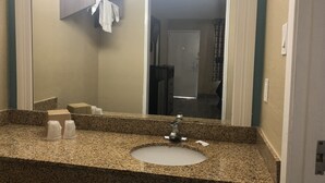 A bathroom with a granite countertop, a sink, a mirror, and a towel rack. - Luxury Inn & Suites (Houston)