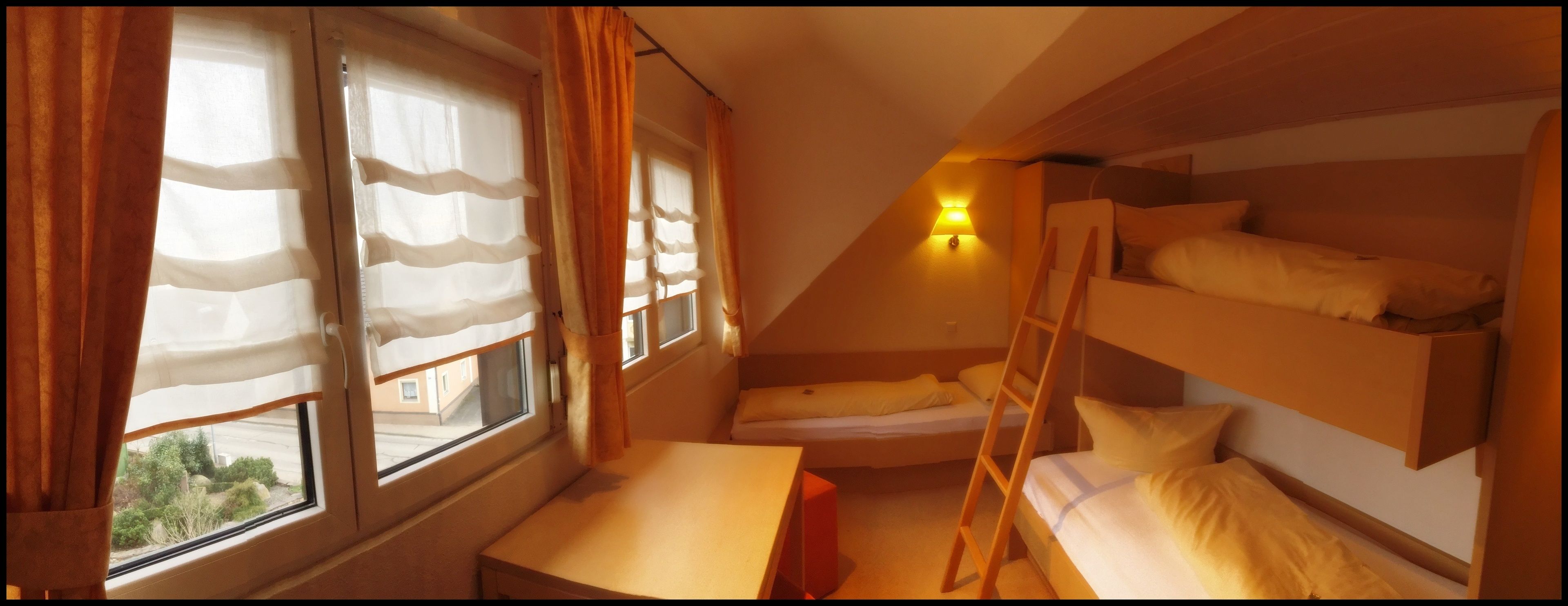 Een studentenkamer met stapelbedden, een bureau en een raam met gordijnen.