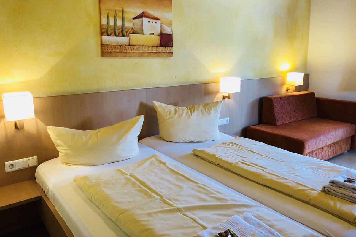 Une chambre d’hôtel avec deux lits, un canapé et deux lampes fixées au mur.
