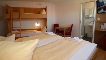 Ein Hotelzimmer mit Etagenbetten, einem Schreibtisch, einem Stuhl und einem durch eine offene Tür einsehbaren Badezimmer.