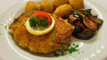 Une assiette contenant une escalope panée, une tranche de citron, du persil et des légumes.