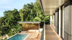 A modern outdoor pool area with wooden loungers, a covered seating area, and lush greenery in the background. - Nikao Luxury Villa (Rarotonga)