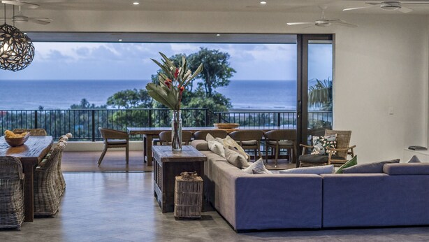A spacious living area with a large sofa, dining table, and chairs, overlooking a scenic ocean view. - Nikao Luxury Villa (Rarotonga)