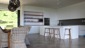 A modern kitchen with white cabinetry, a central island with stools, and a dining area with wicker furniture. - Nikao Luxury Villa (Rarotonga)