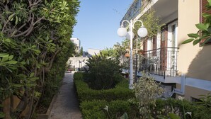 A narrow pathway flanked by lush greenery and a building with balconies and outdoor lighting fixtures. - L'Officina di Apollo (Palermo)