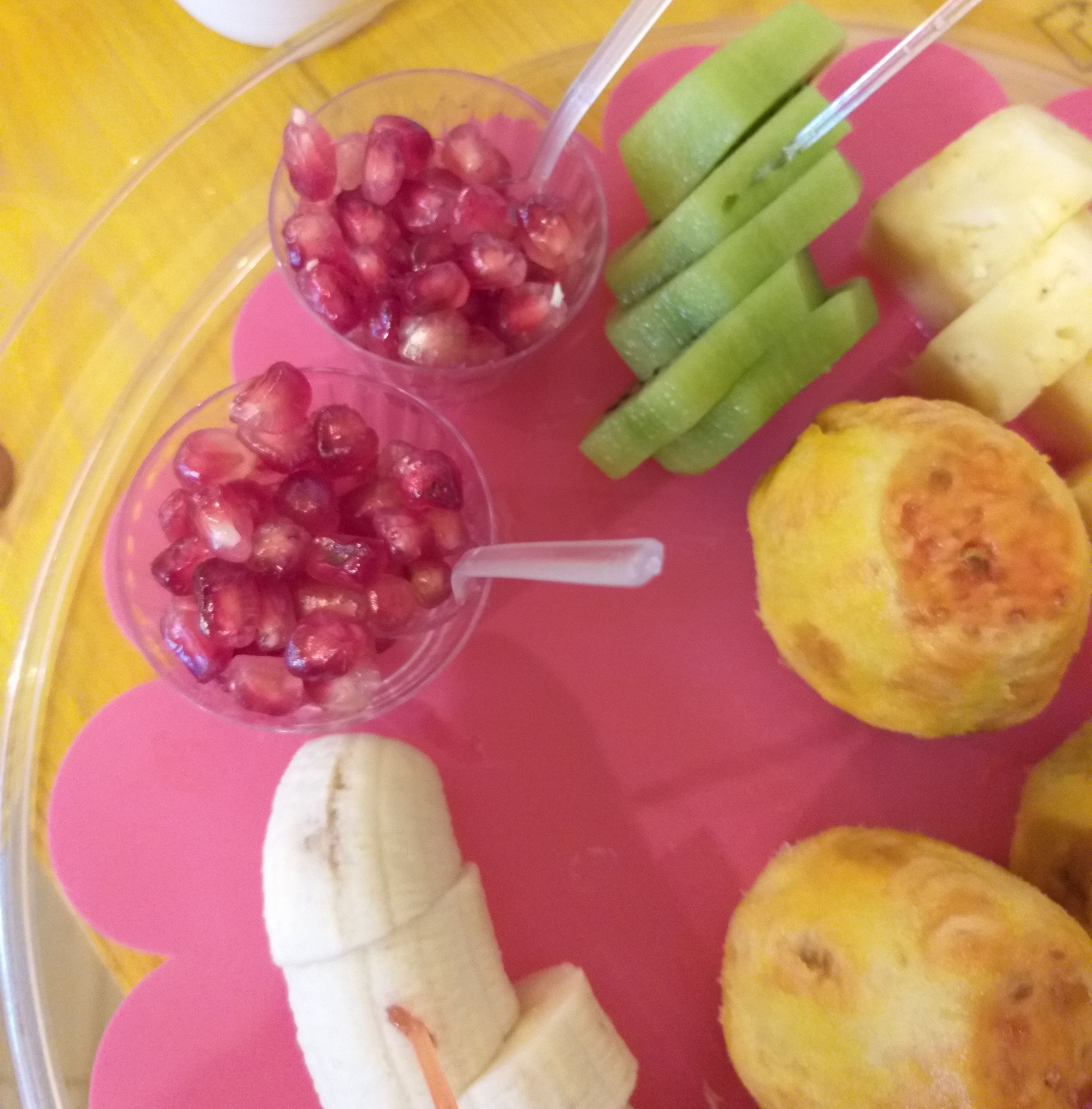Ein Teller mit Granatapfelkernen, Gurkenscheiben, einer Banane und zwei kleinen Gebäcken.