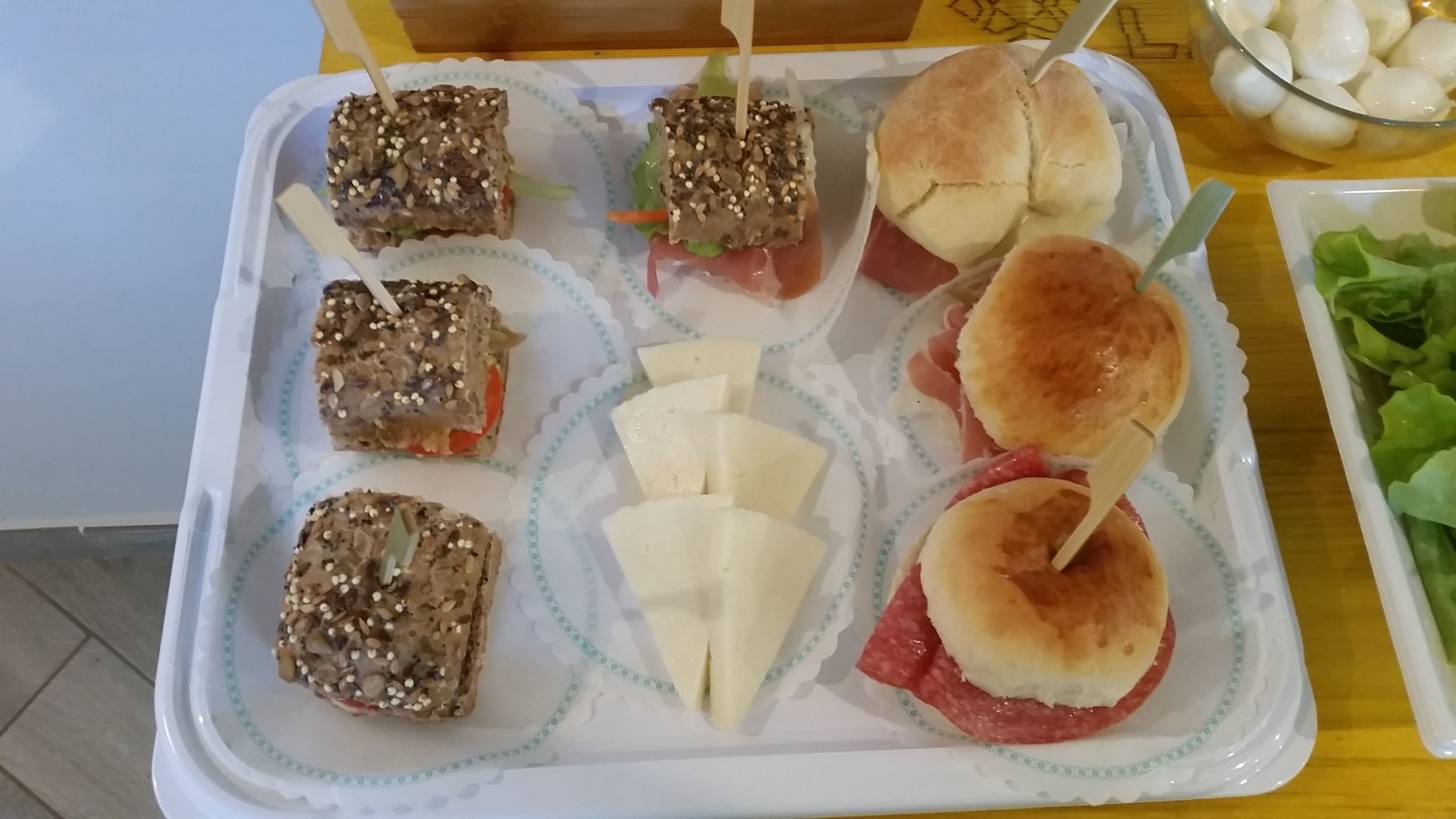 Una bandeja con diferentes alimentos, como sándwiches, una ensalada y un tazón con lo que parecen albóndigas.