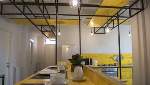 A modern kitchen with yellow accents, a wooden dining table set for two, and a view into the adjacent dining area. - L'Officina di Apollo (Palermo)