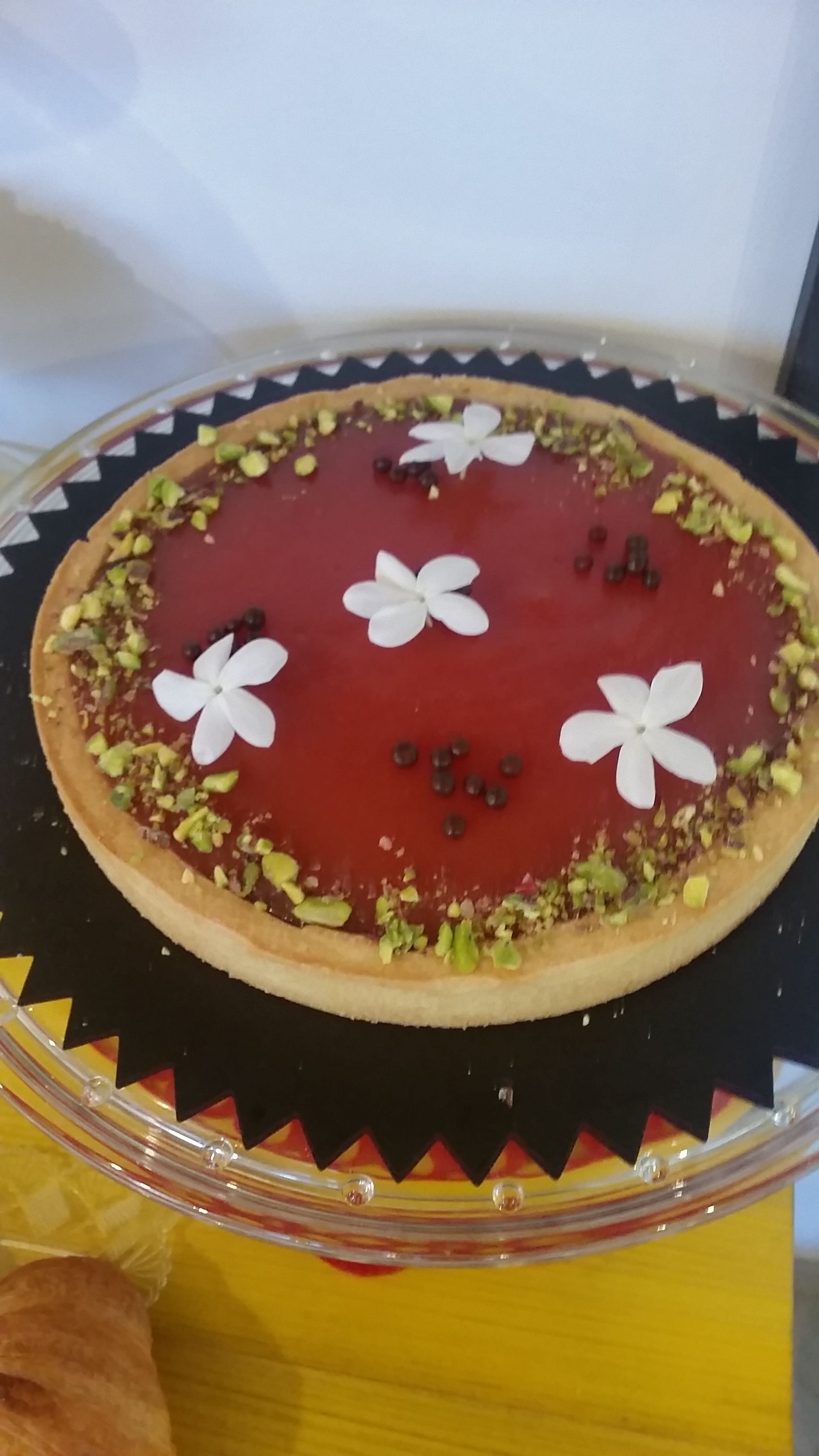 Un postre con cobertura roja, flores blancas y trozos de pistacho verde sobre un plato.