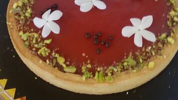Un postre con cobertura roja, flores blancas y trozos de pistacho verde sobre un plato.