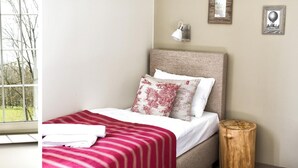 A neatly made bed with a striped red and white bedspread, a wooden nightstand, and a window with curtains.