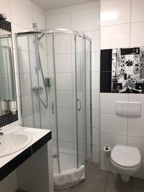A bathroom with a glass-enclosed shower, a white sink, a toilet, and a tiled wall with a black and white pattern. - Dom M Cynarza (Pruszcz Gdański)