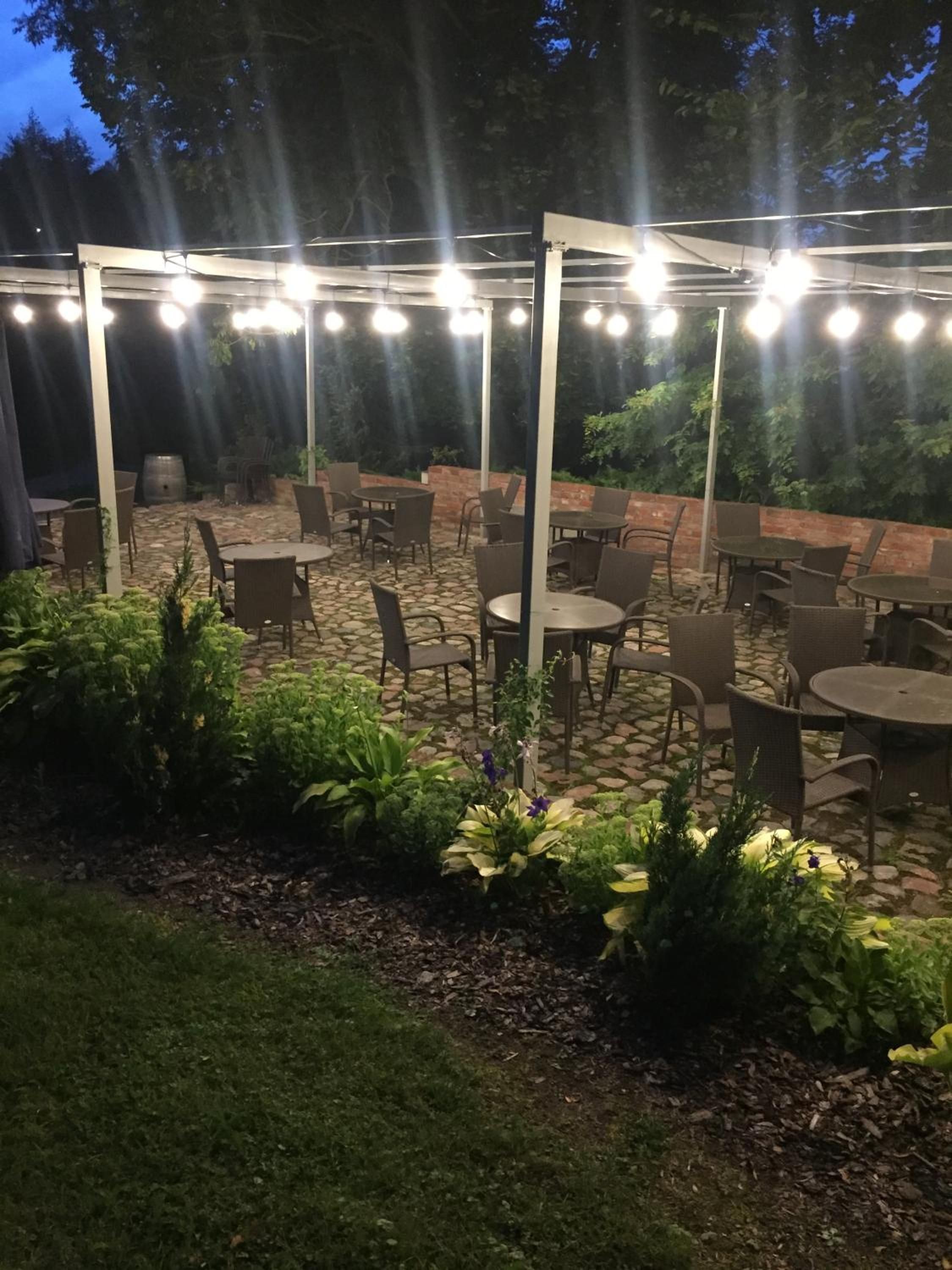 Un patio al aire libre con mesas y sillas, rodeado de vegetación y un muro de ladrillo.