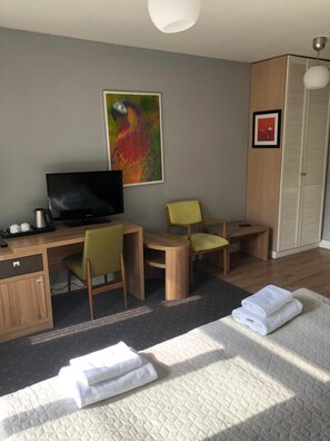 A hotel room with a bed, a desk with a television, two chairs, a wardrobe, and a painting on the wall.