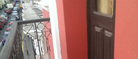 A narrow balcony with a red wall and a brown door.