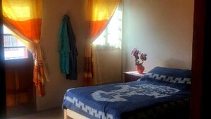 Un dormitorio con cama, ventana con cortinas, una silla y una mesa.