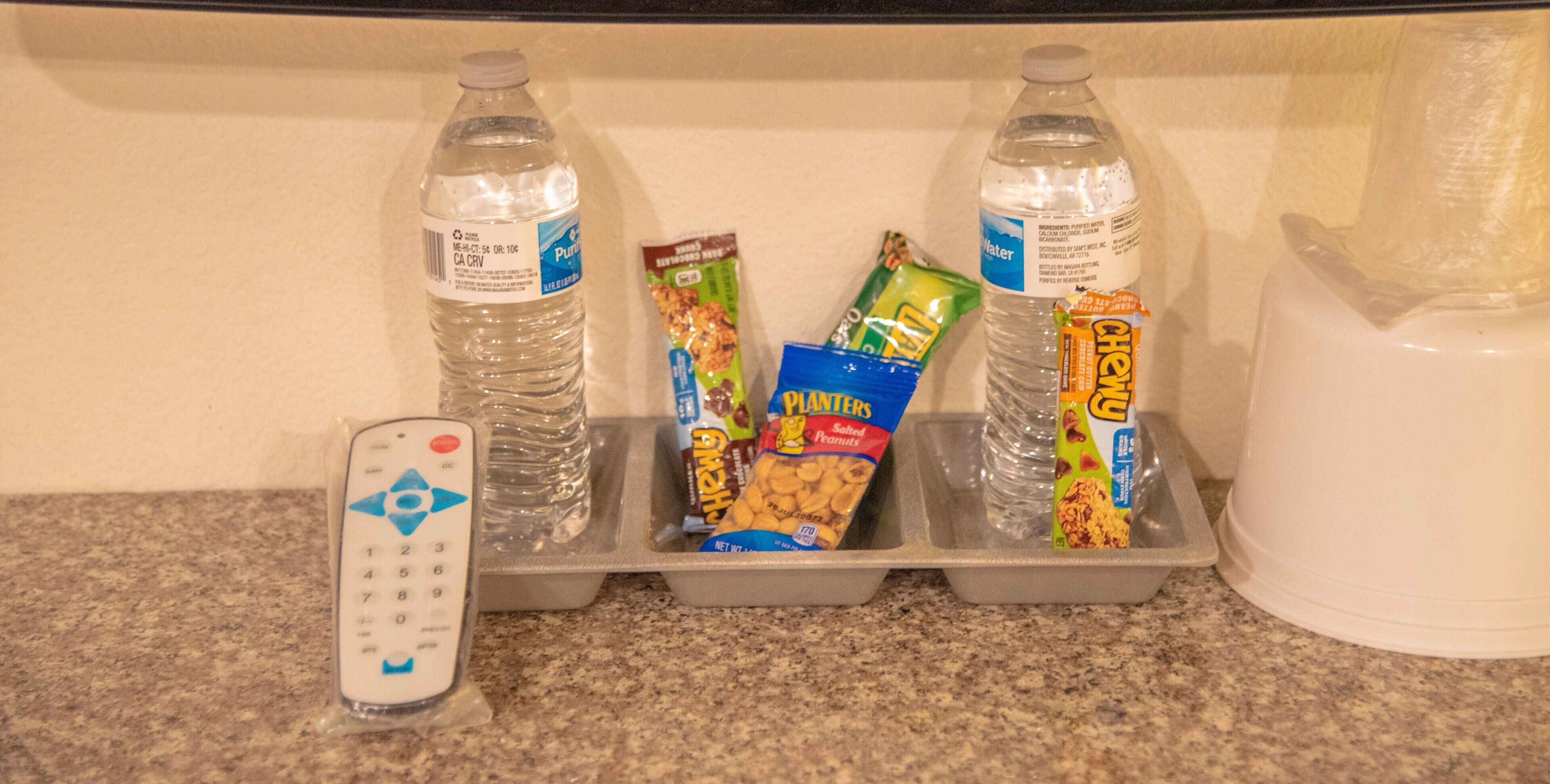 A tray with snacks, two bottles of water, and a remote control on a kitchen counter.