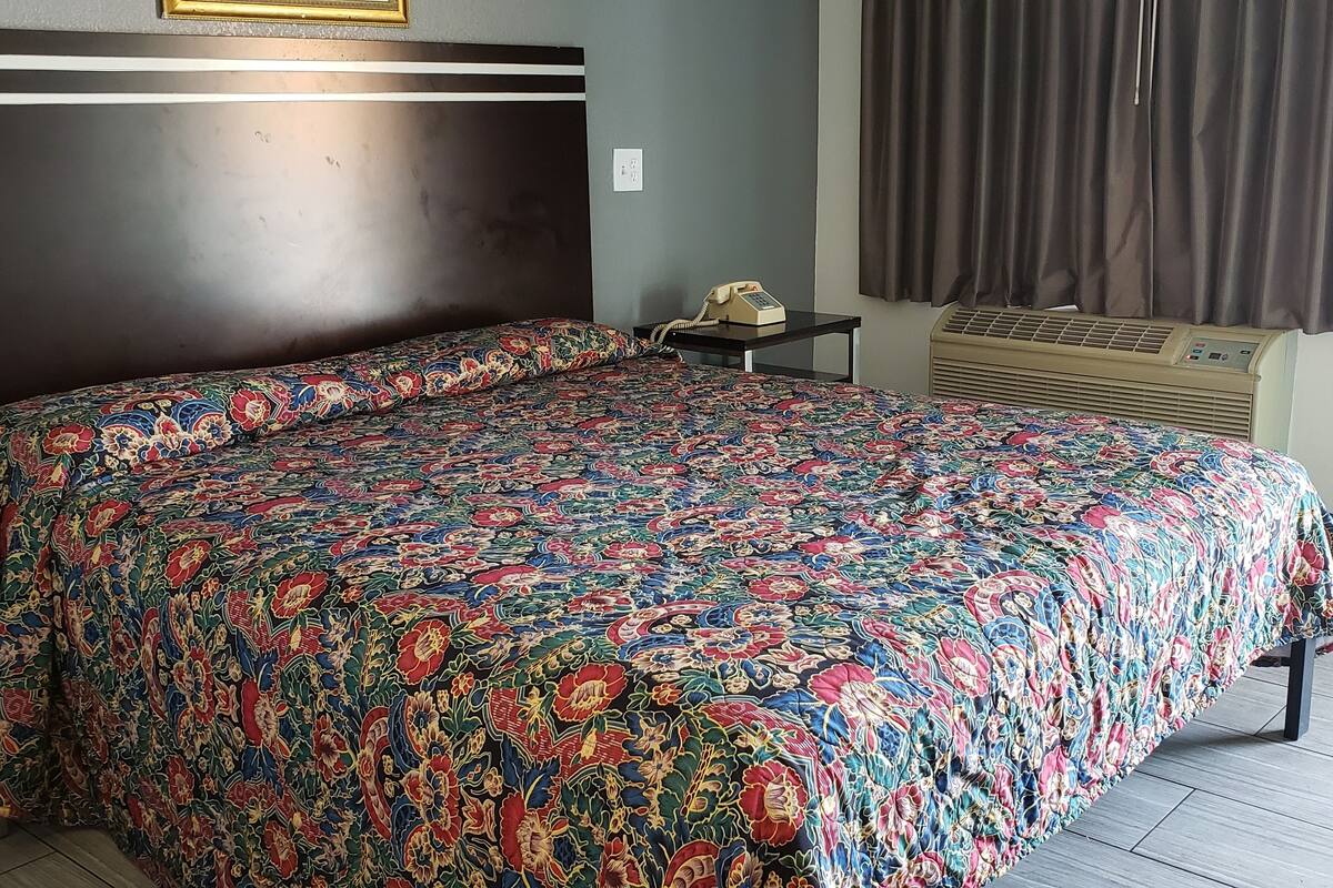 A neatly made bed with a patterned bedspread, a bedside table with a telephone, and an air conditioning unit on the wall.