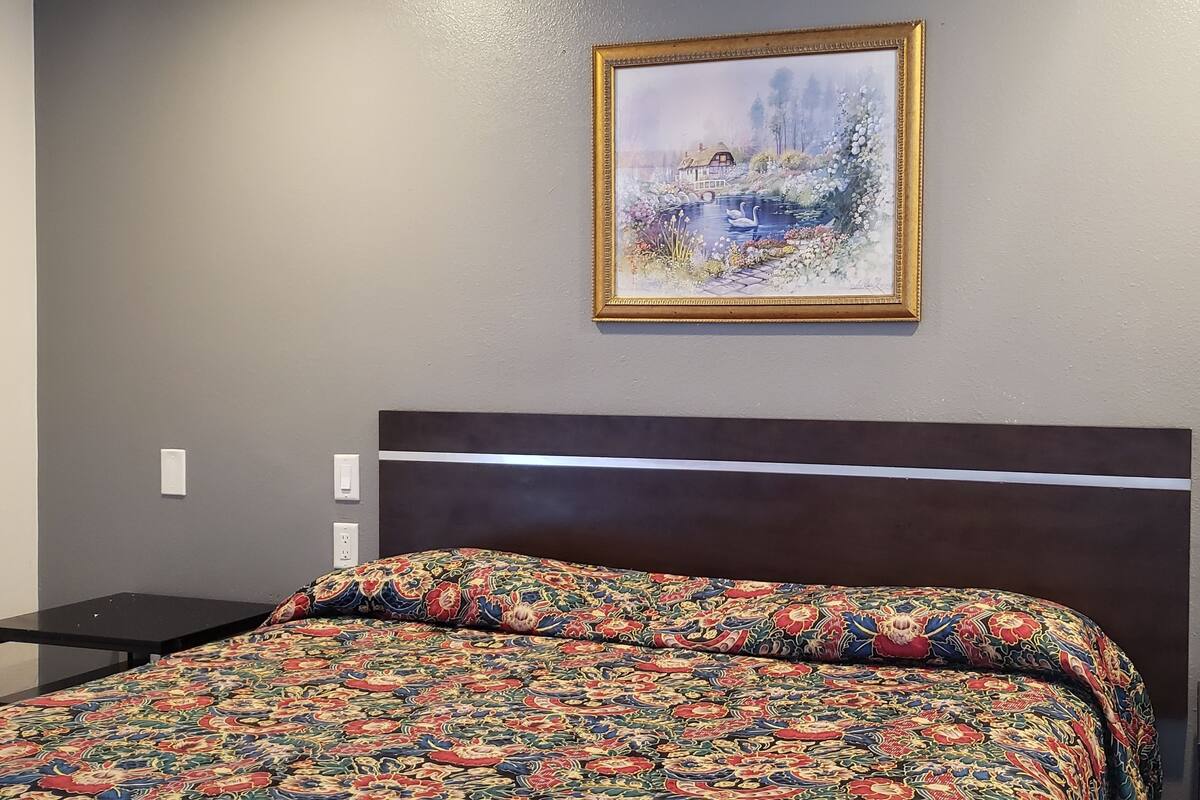 A hotel room with a bed, a nightstand with a phone, and a painting on the wall.