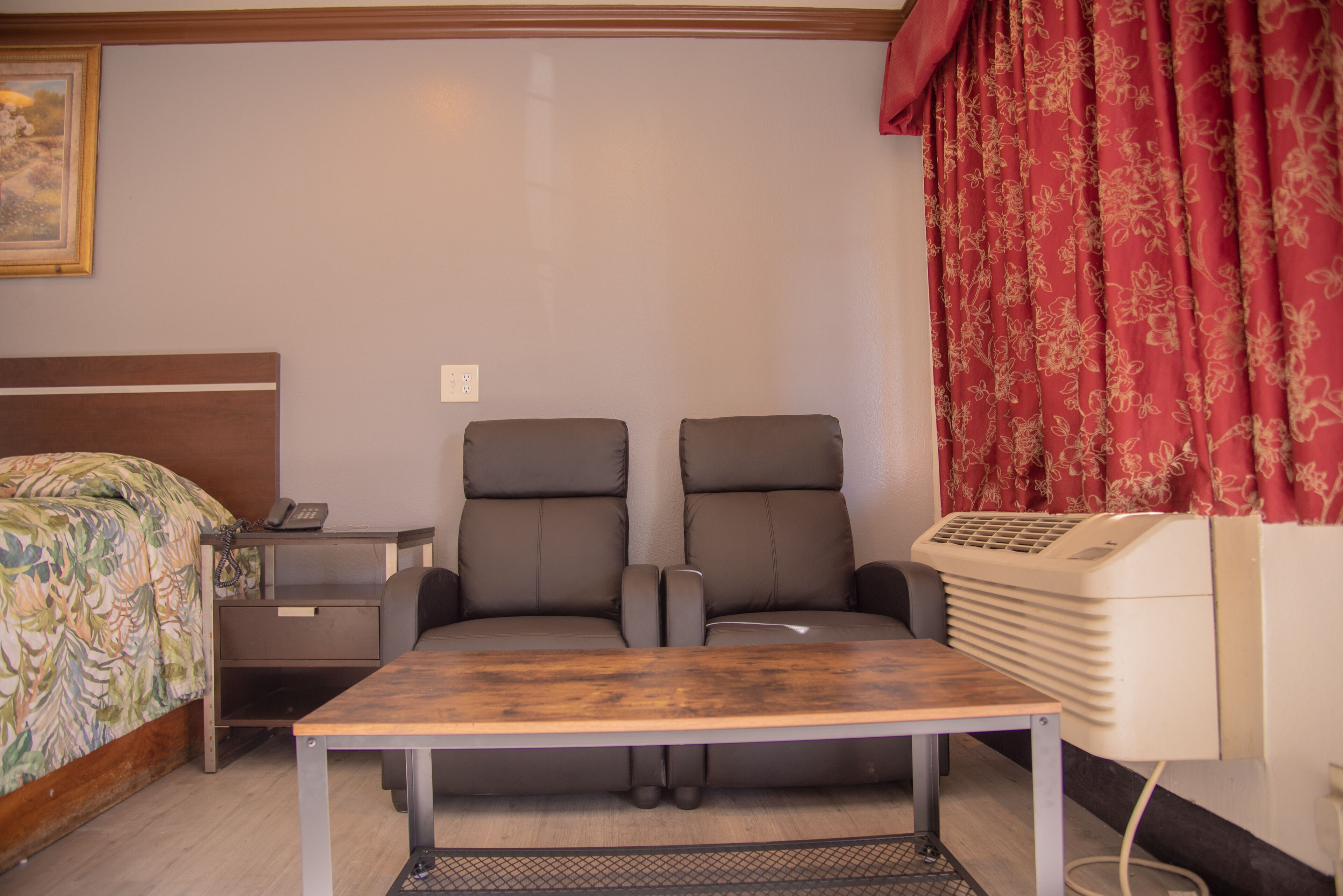 A hotel room with a bed, two reclining chairs, a small table, a desk, and a heater.