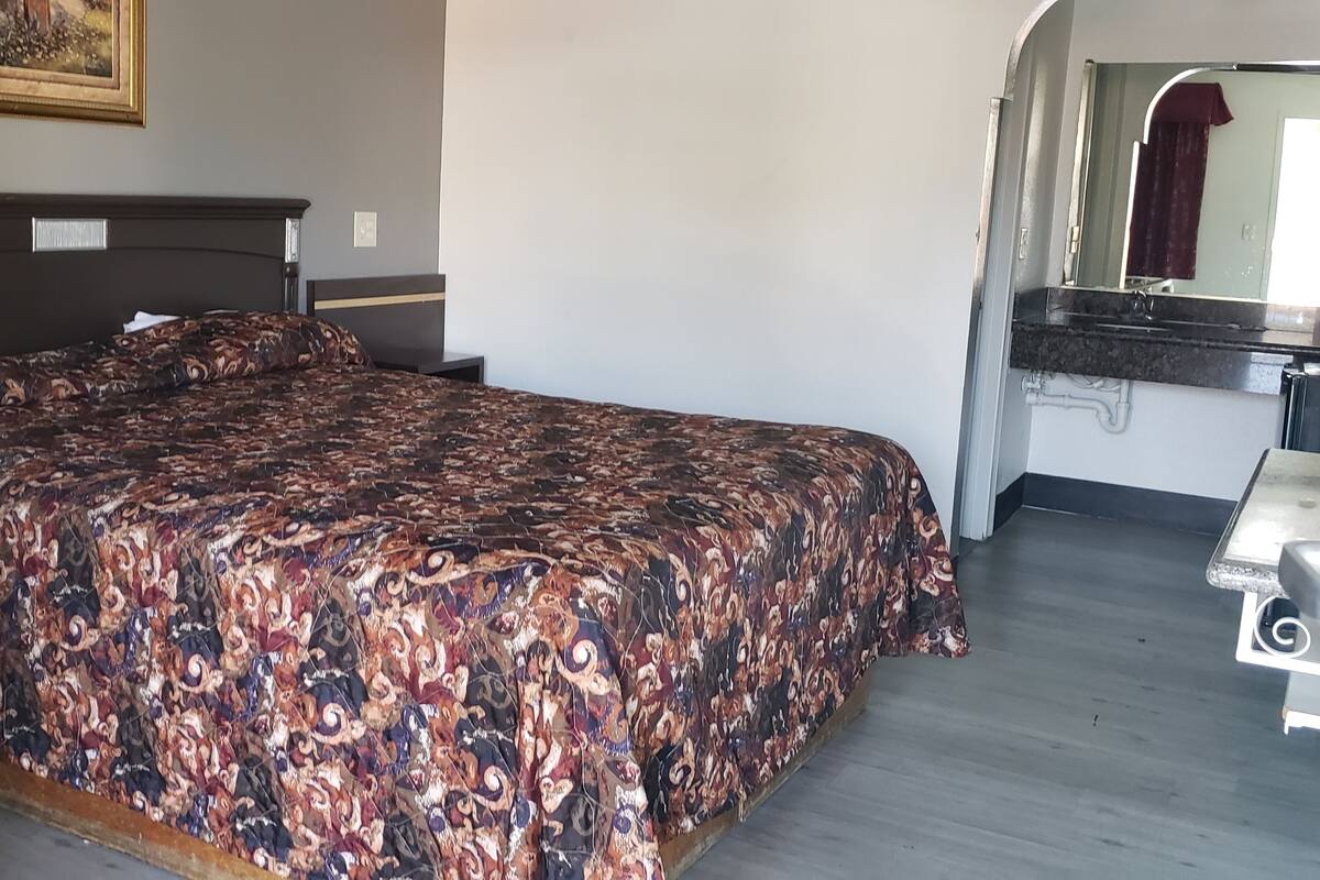 A bedroom with a large bed, a bedside table, a mirror, and a bathroom with a sink and mirror.