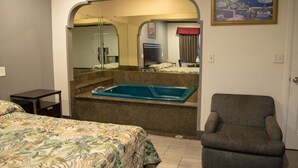 Ein Hotelzimmer mit einem Bett, einem Sessel, einer Badewanne und einem Bild an der Wand.