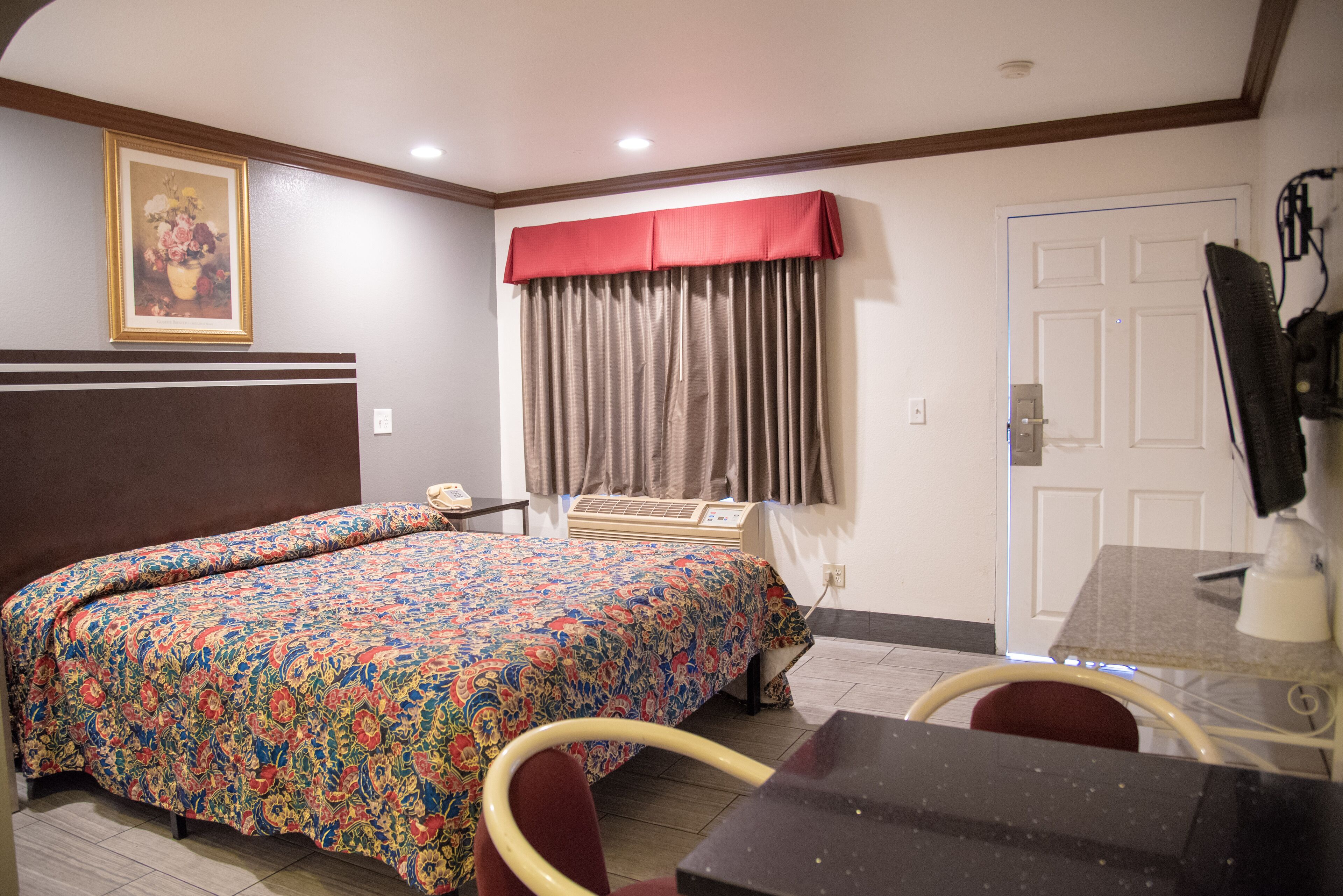 A hotel room with a bed, a desk, a chair, a TV, and a door.