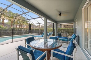 Un espace extérieur abrité, doté d’une table et de chaises en verre, d’une piscine et offrant une vue sur des palmiers.