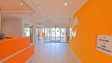 A reception area with orange seating, a glass door entrance, and directional signage.