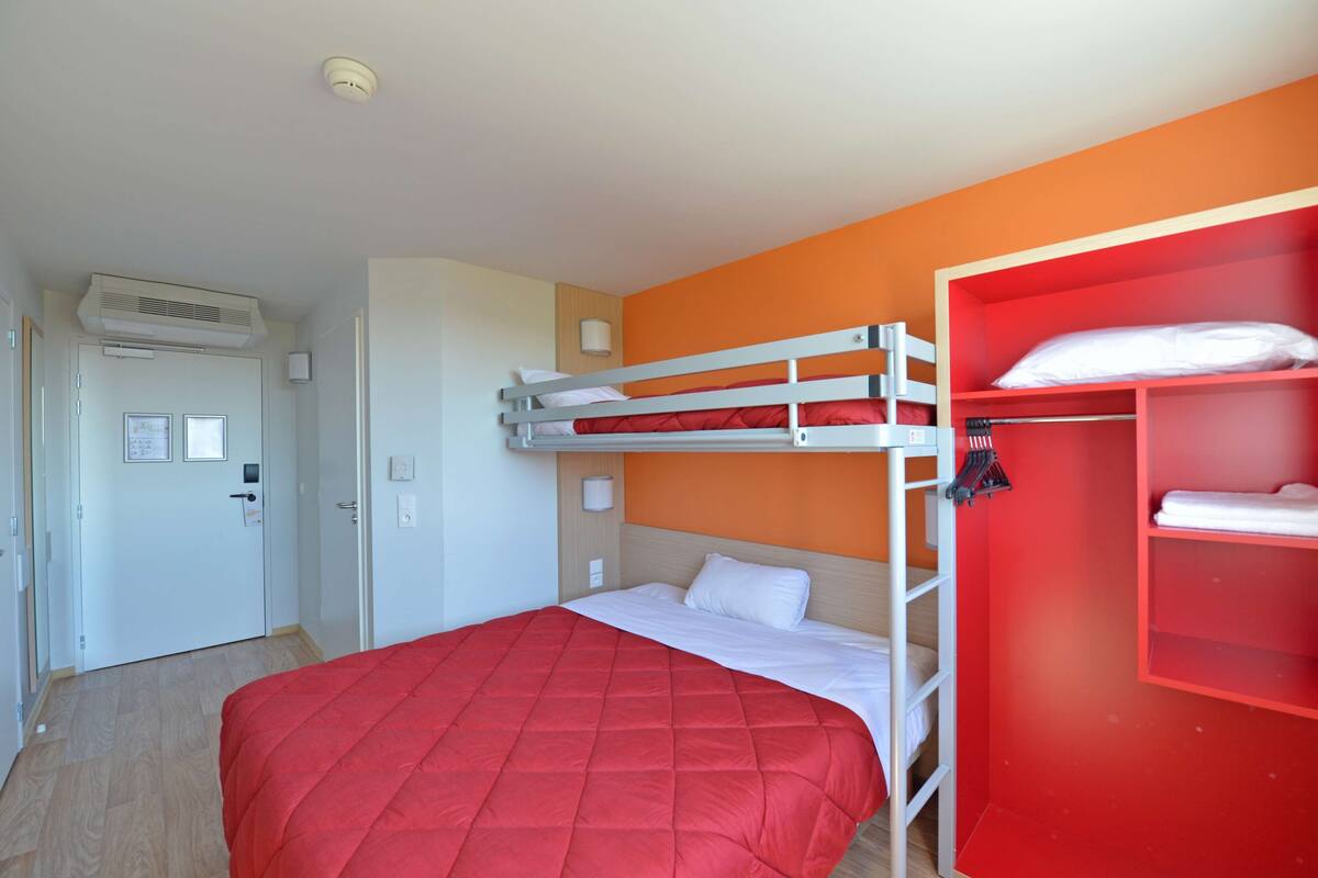 Ein Hotelzimmer mit Etagenbett, einem roten Kleiderschrank und einer Tür mit Lichtschalter und kleinem Schild.