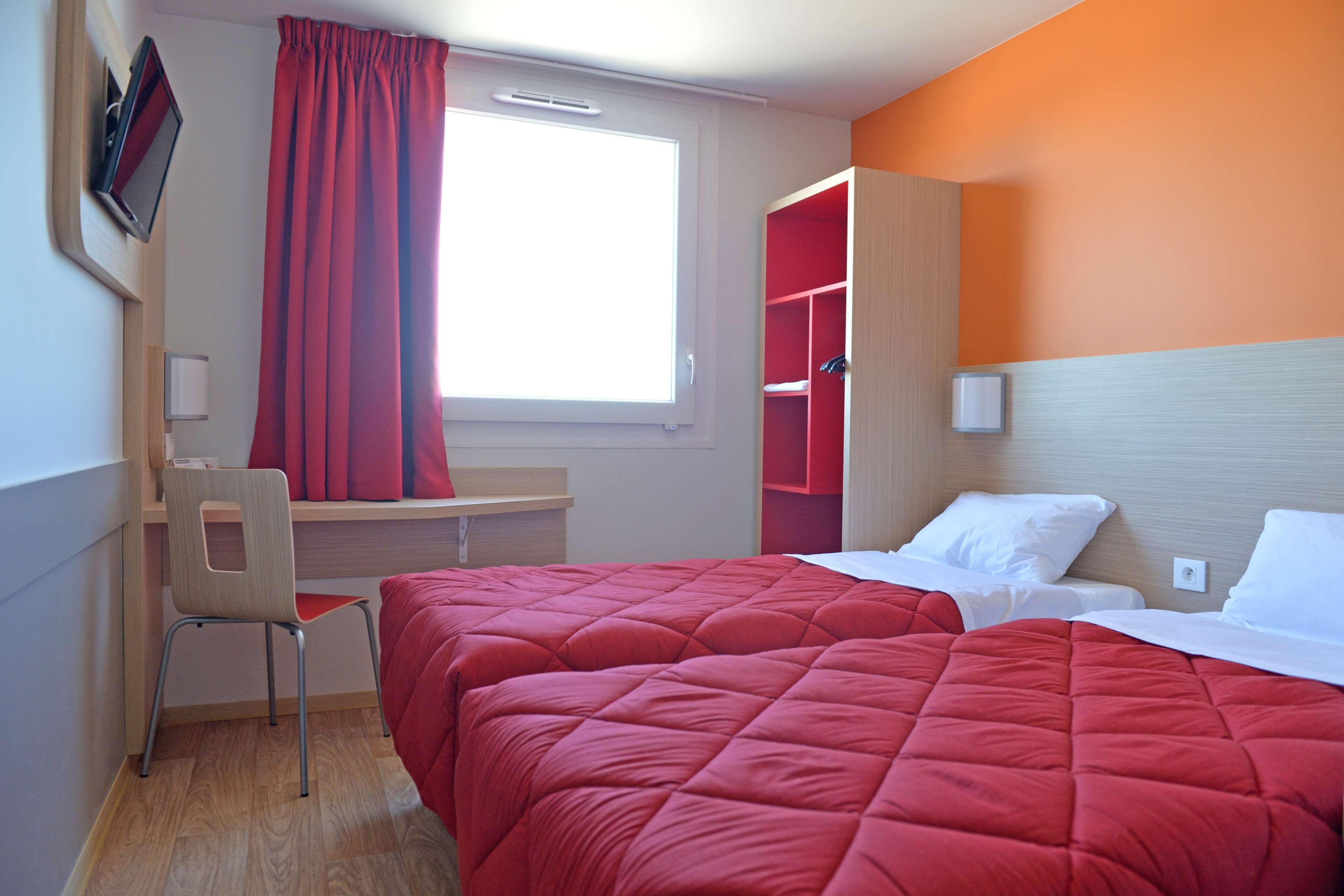 Quarto de hotel com duas camas, uma escrivaninha, uma cadeira e uma televisão.