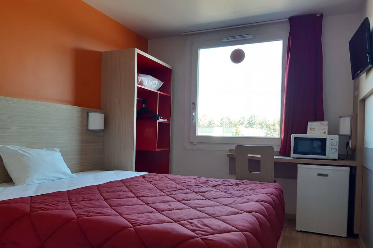 Ein Hotelzimmer mit Bett, Schreibtisch, Mikrowelle, kleinem Kühlschrank und einem Fenster mit Vorhängen.