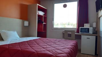 Habitación de hotel con cama, escritorio con microondas, refrigerador pequeño y ventana con cortinas.