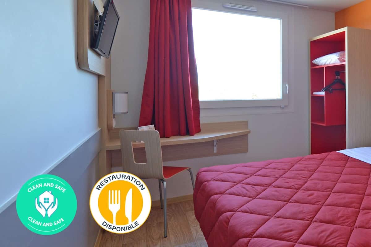 Ein Hotelzimmer mit einem Bett, einem Schreibtisch, einem Stuhl, einem Fernseher und einem Fenster mit roten Vorhängen.