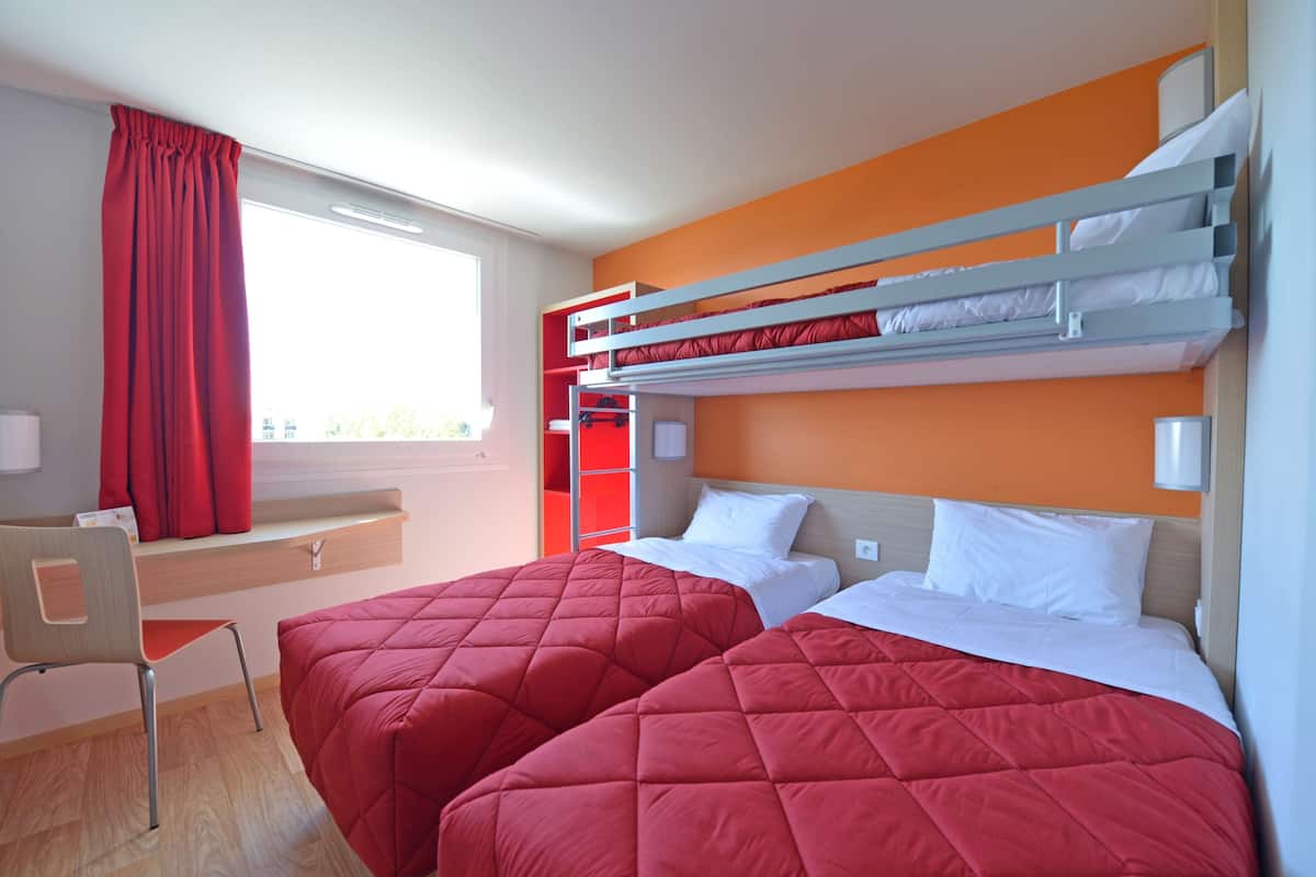 Ein Hotelzimmer mit zwei Betten, einem Schreibtisch und einem Fenster mit Vorhängen.
