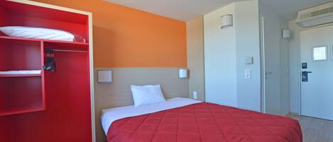 Una habitación de hotel con una colcha roja, una almohada blanca, un armario rojo y una puerta blanca.
