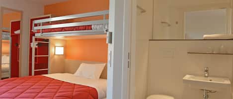 Une chambre d’hôtel avec un lit superposé, un lit simple, une salle de bain avec un lavabo et des toilettes, et un miroir au-dessus du lavabo.