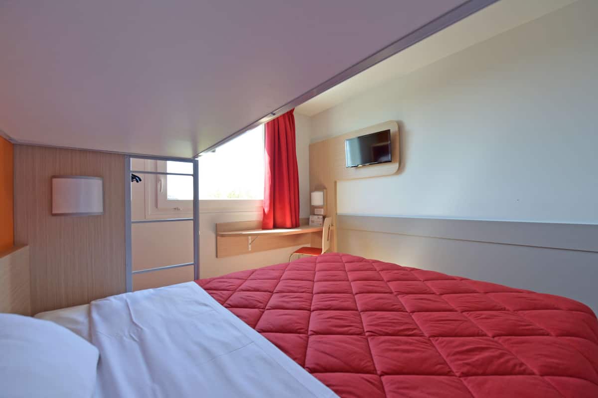 Ein Hotelzimmer mit einem Bett, einem Schreibtisch, einem Sessel, einem Fernseher und einem Fenster mit Vorhängen.