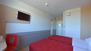 Una habitación de hotel con una cama, un televisor en la pared, una silla roja y un escritorio.