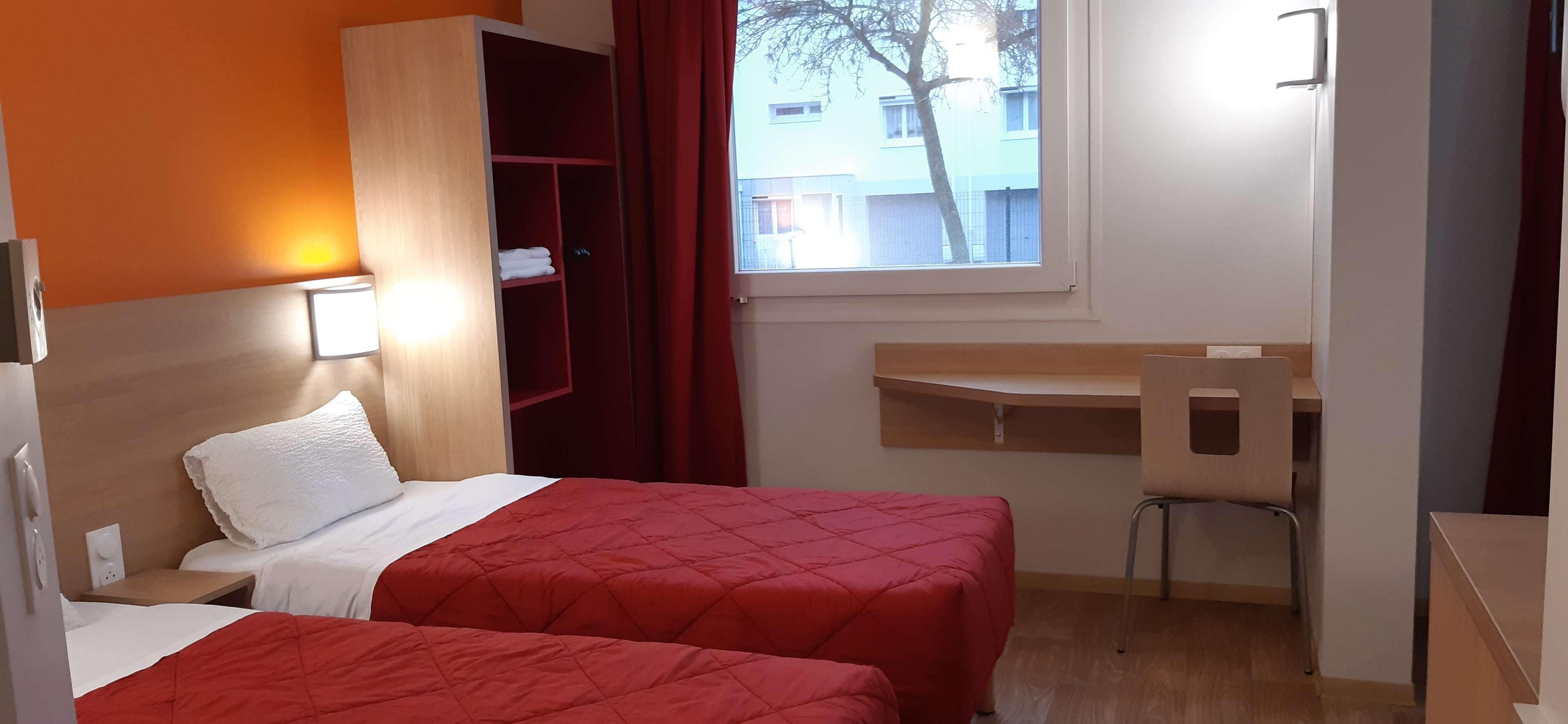 Een hotelkamer met twee bedden, een bureau en een stoel.
