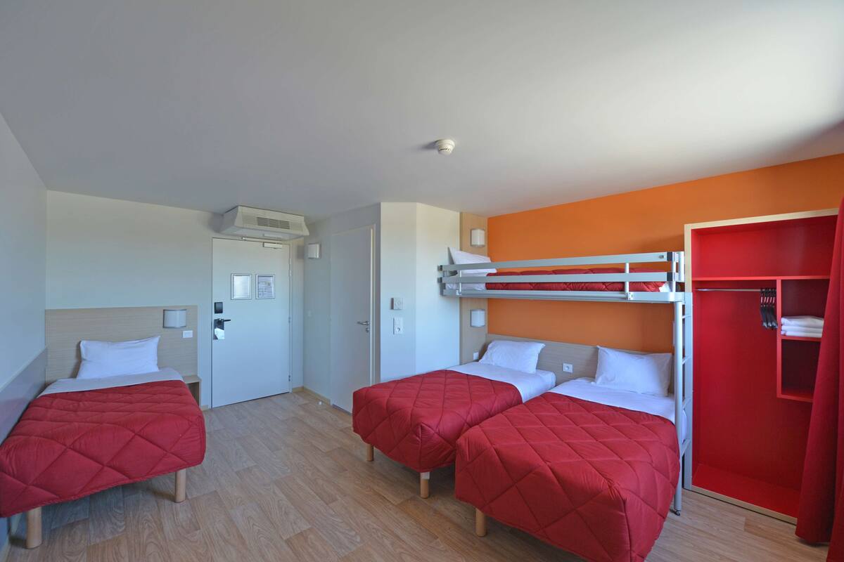 Ein Hotelzimmer mit zwei Einzelbetten, einem Etagenbett und einem roten Kleiderschrank.