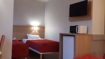 A compact hotel room with a bed, a desk with a microwave, a TV mounted above the desk, and a small refrigerator.